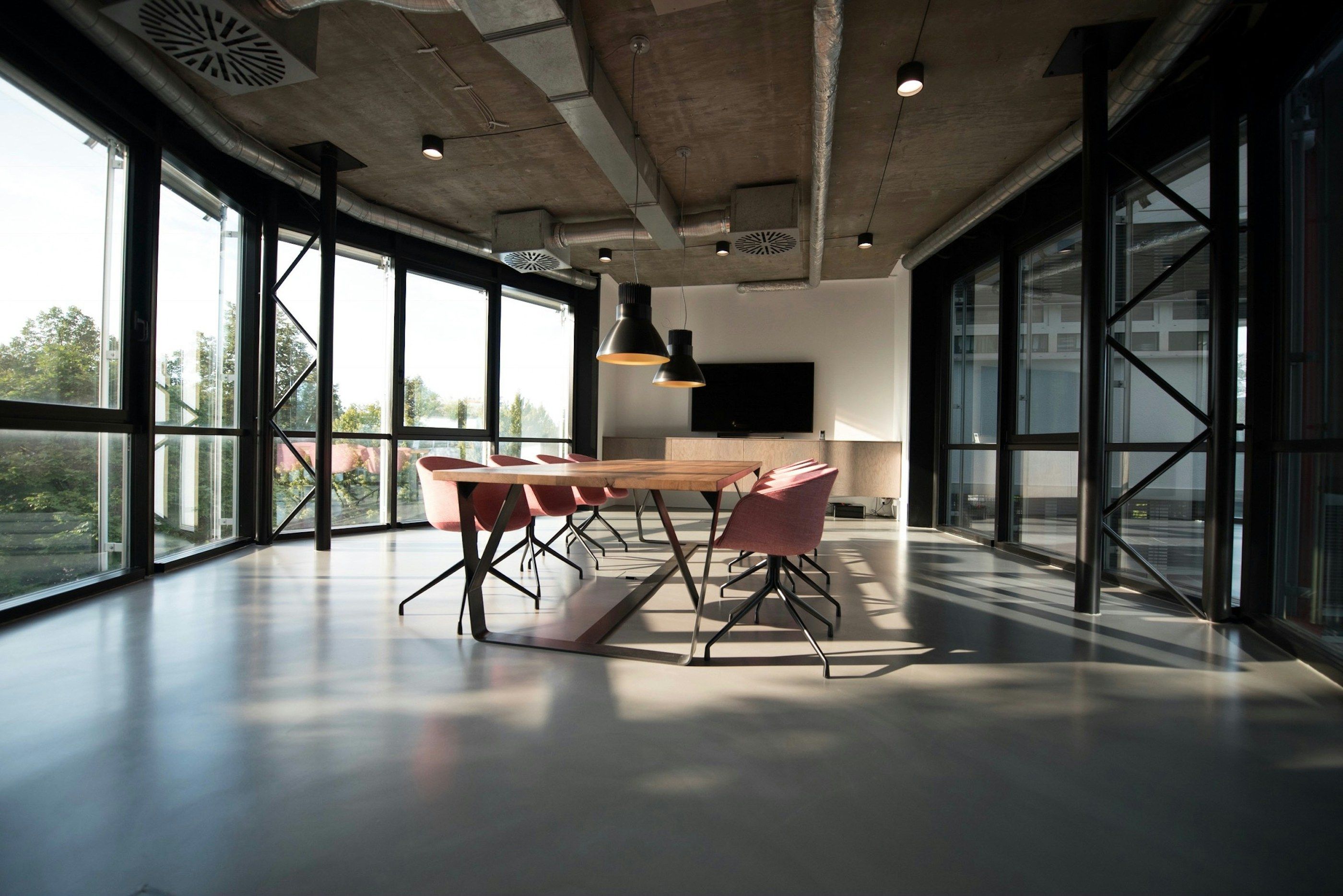 A spacious, sunlit boardroom with a long table, chairs and floor-to-ceiling windows